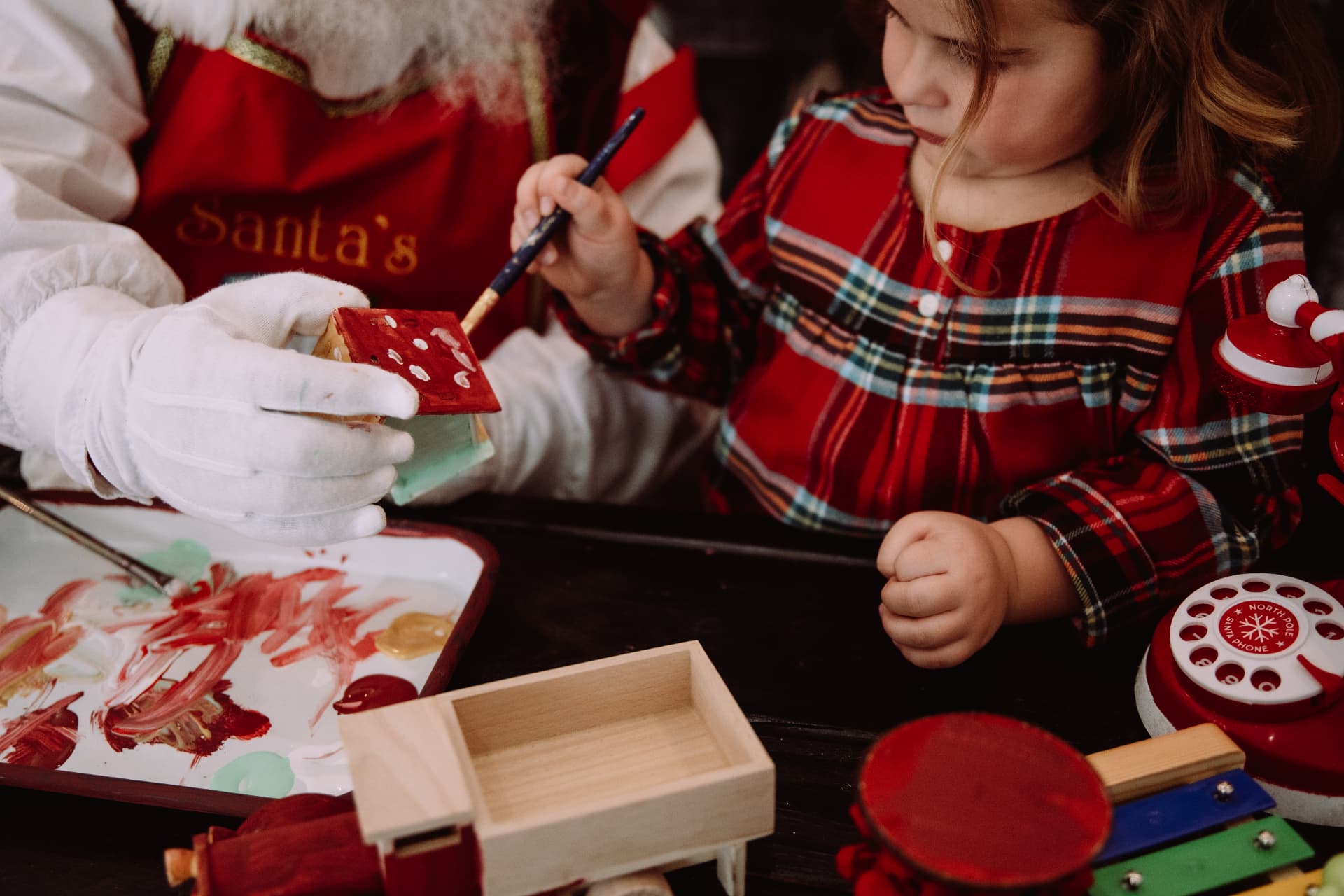Close-up of a child's hand painting a wooden birdhouse red with Santa