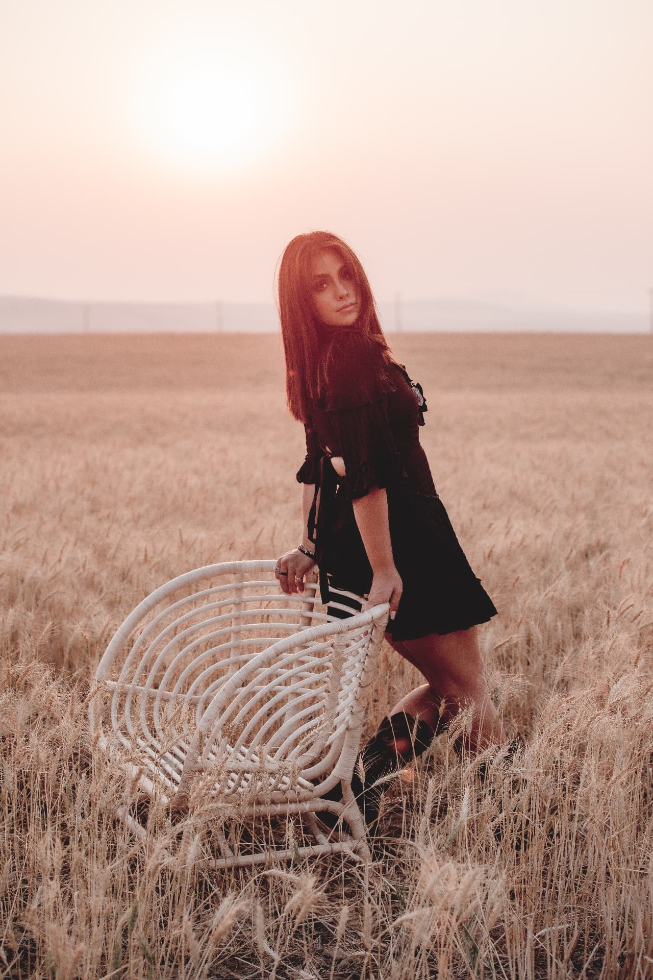 Senior at sunset with a white rattan chair in the wheat