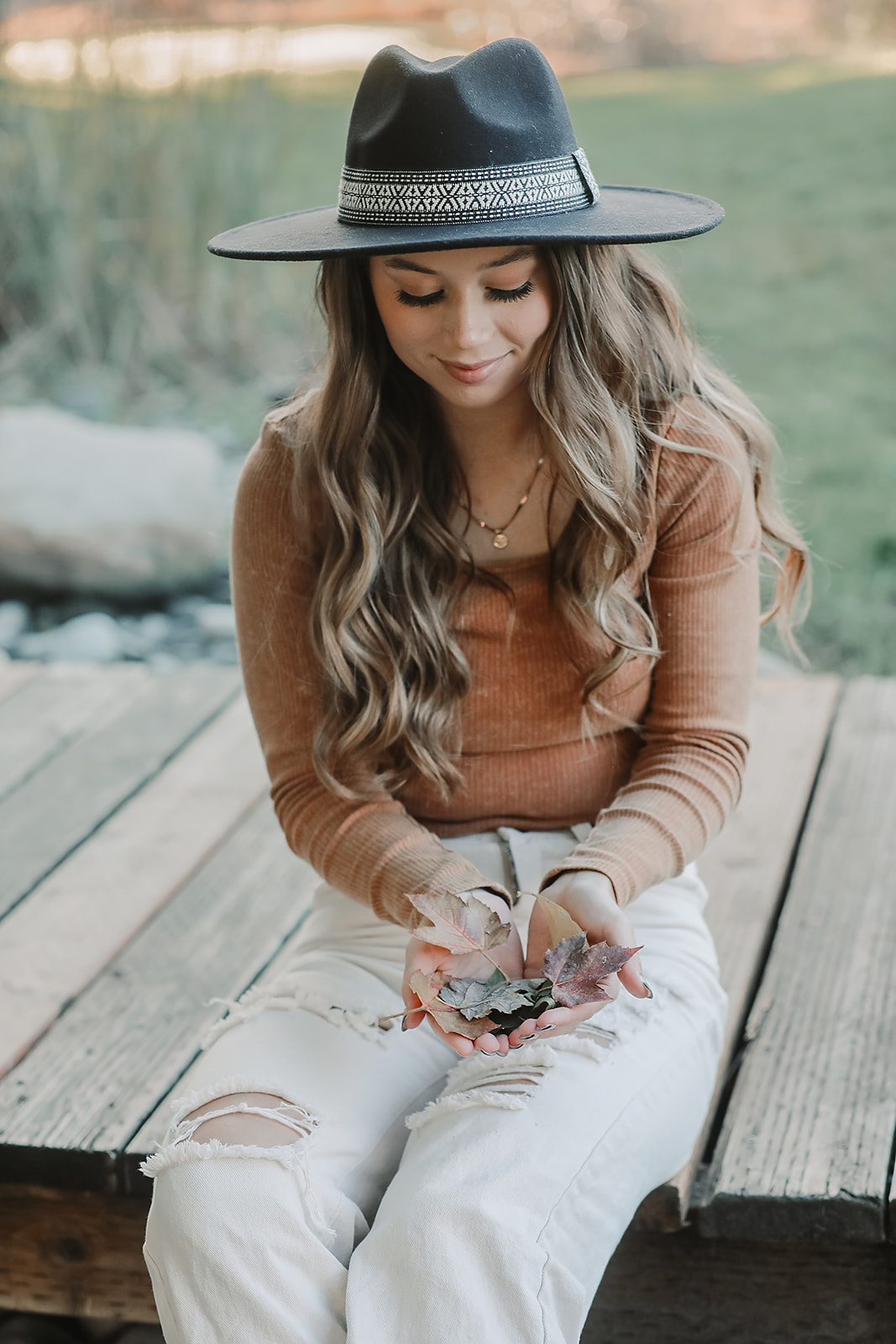 Senior holding fallen autumn leaves while seated on a wooden bridge