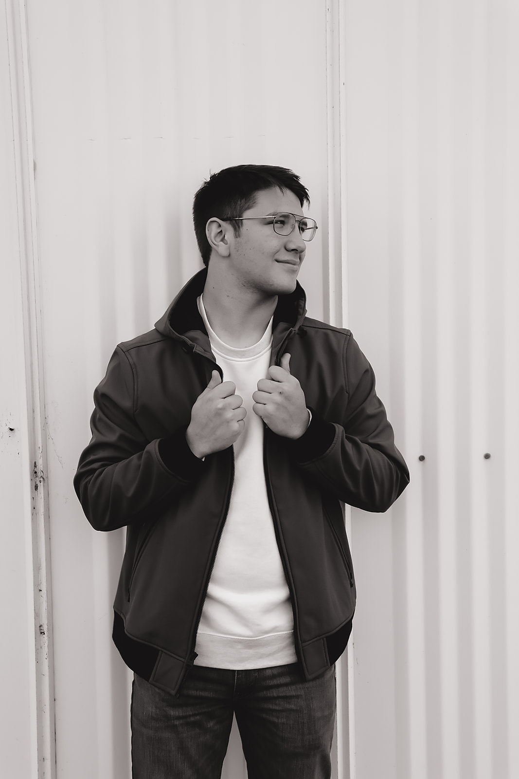 Black and white senior portrait of a young man in a bomber jacket against a white wall