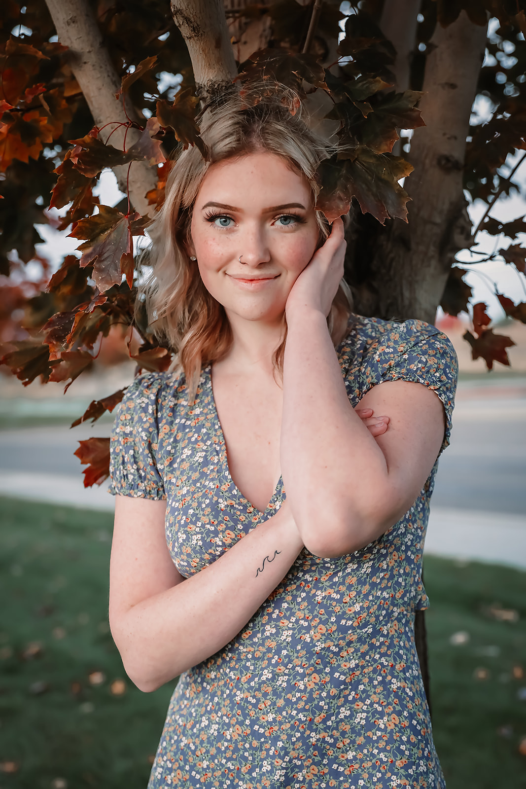 Senior in a floral dress beneath autumn maple leaves