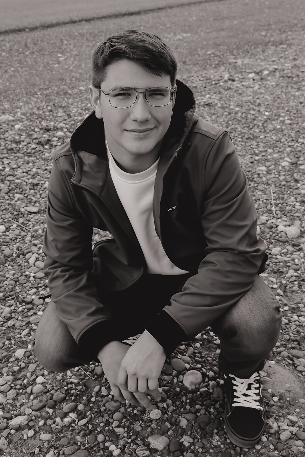 Black and white senior portrait crouched on a gravel road