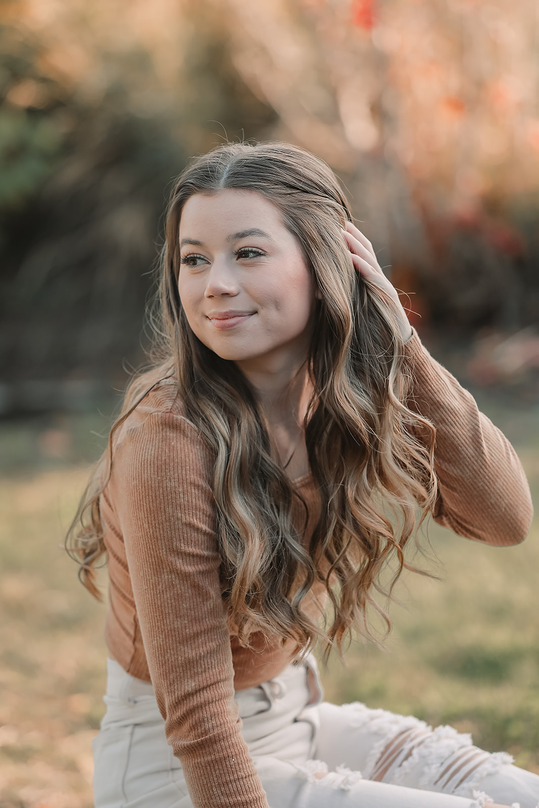 Senior brushing her hair back in front of glowing autumn foliage