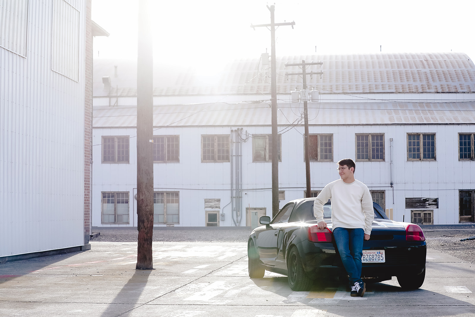 Senior leaning against a black sports car in backlit sunlight