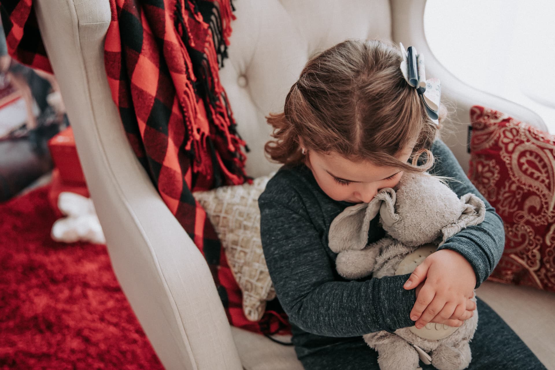 Little girl snuggling her lamb stuffed animal in a cozy plaid Christmas chair