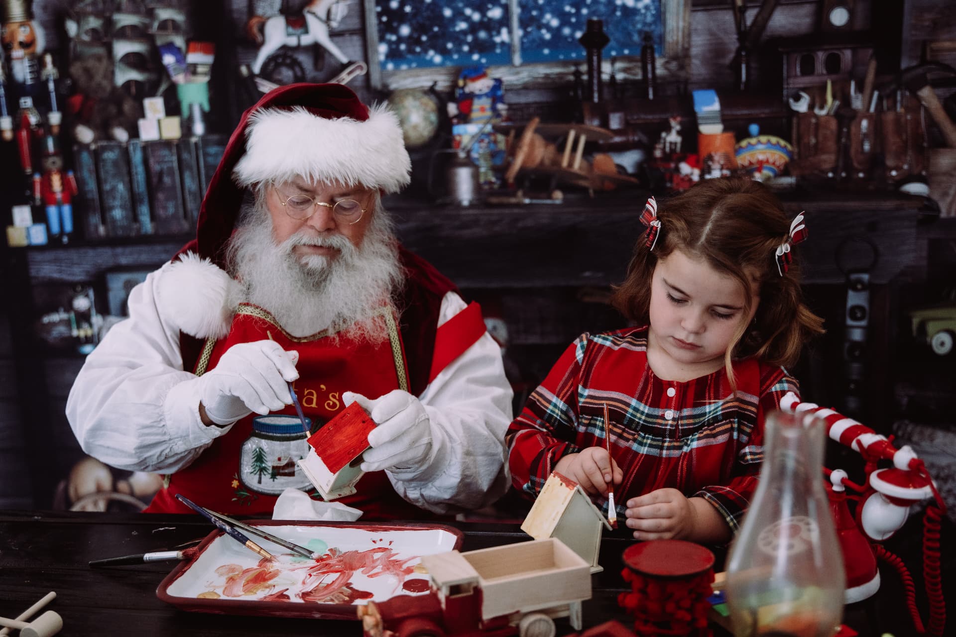Santa and a little girl in plaid painting wooden birdhouses together