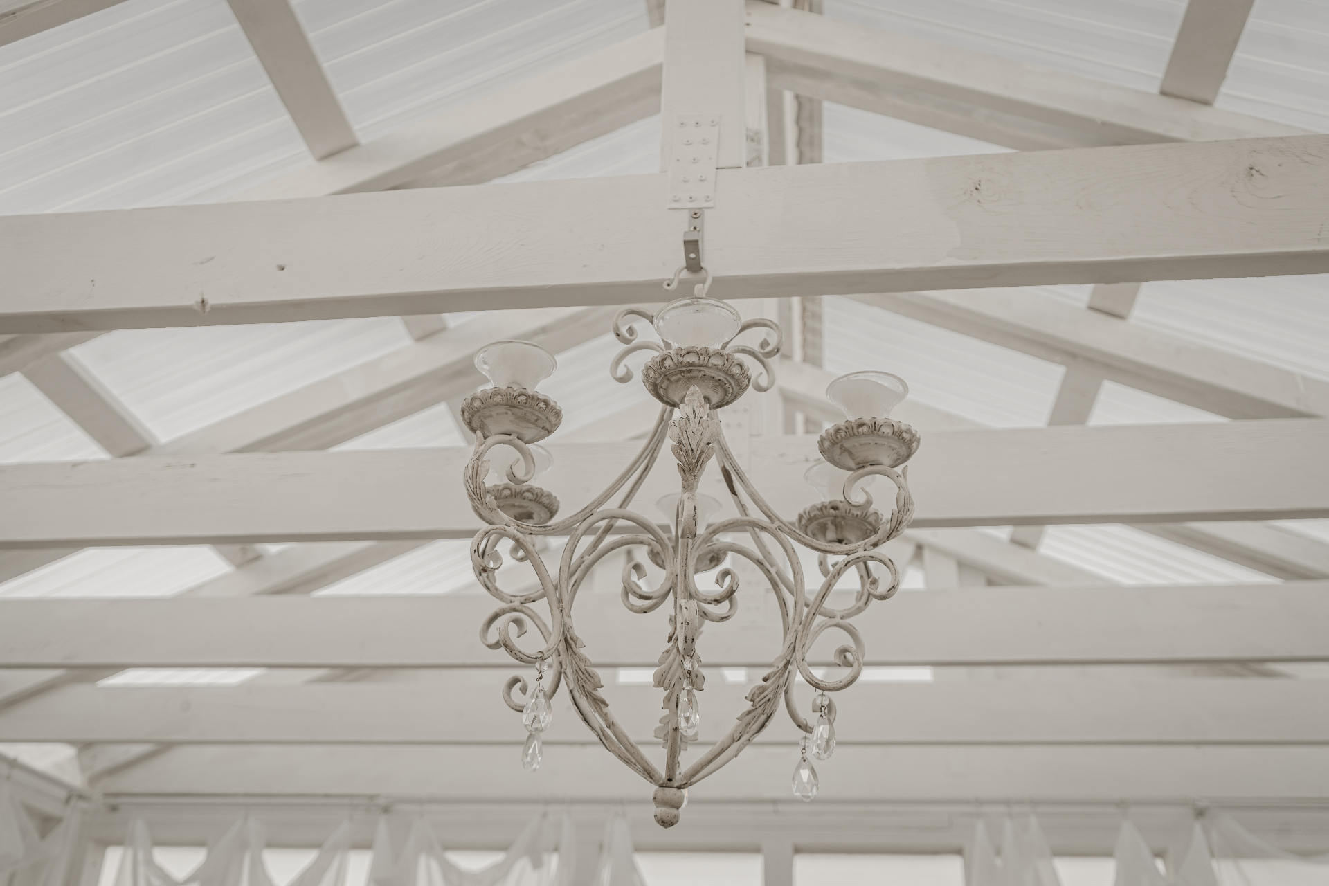 Ornate cream chandelier under sunlit rafters