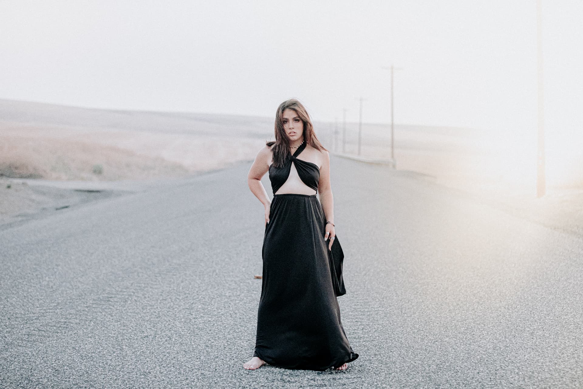 Senior in a long black gown standing on a hazy highway
