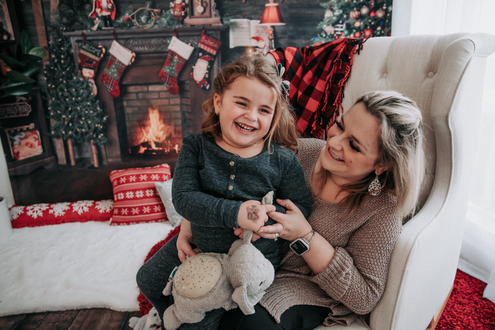 Mother and daughter laughing together beside a Christmas fireplace