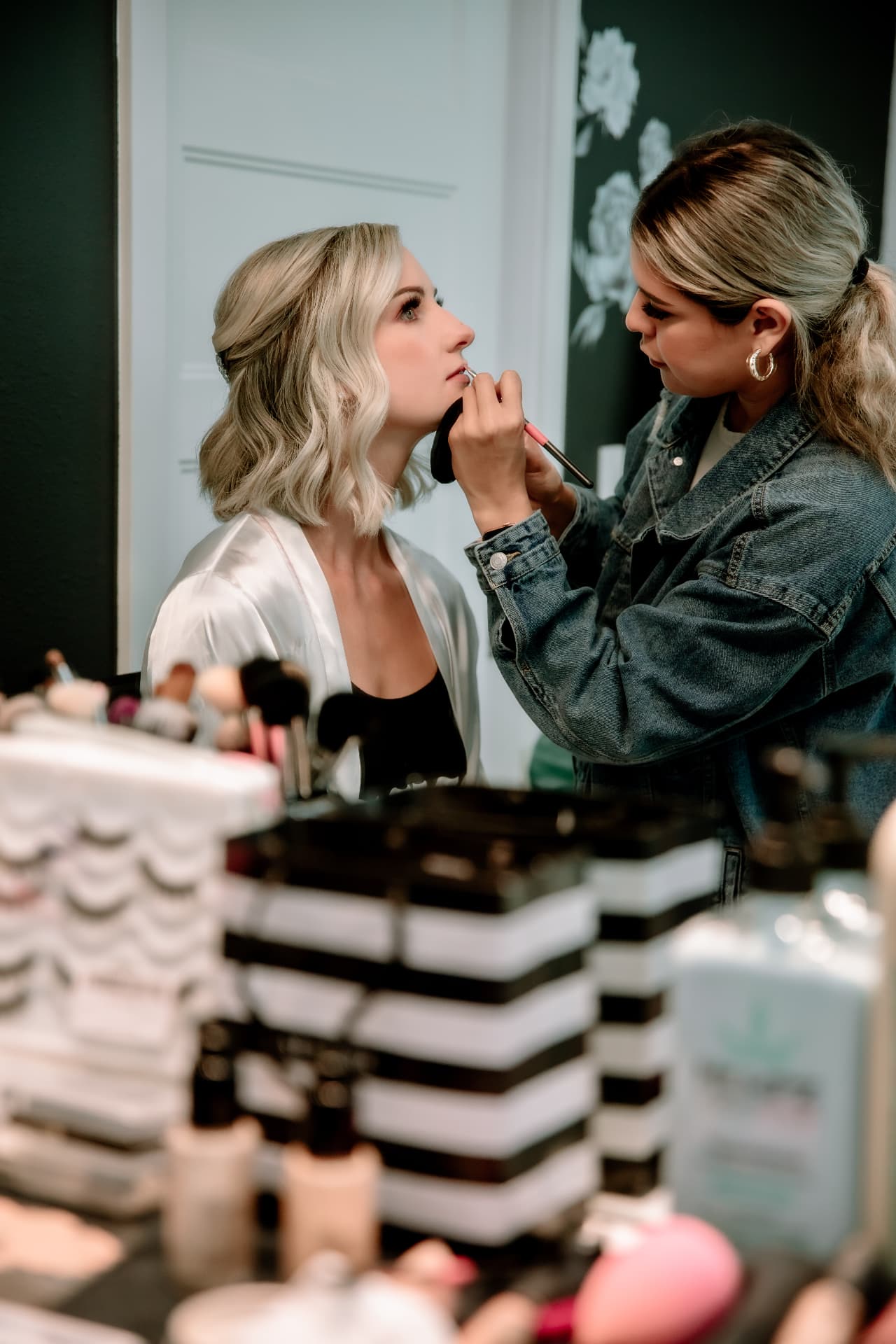 Bride in ivory silk robe having bridal makeup applied inside Glam Studios before her wedding