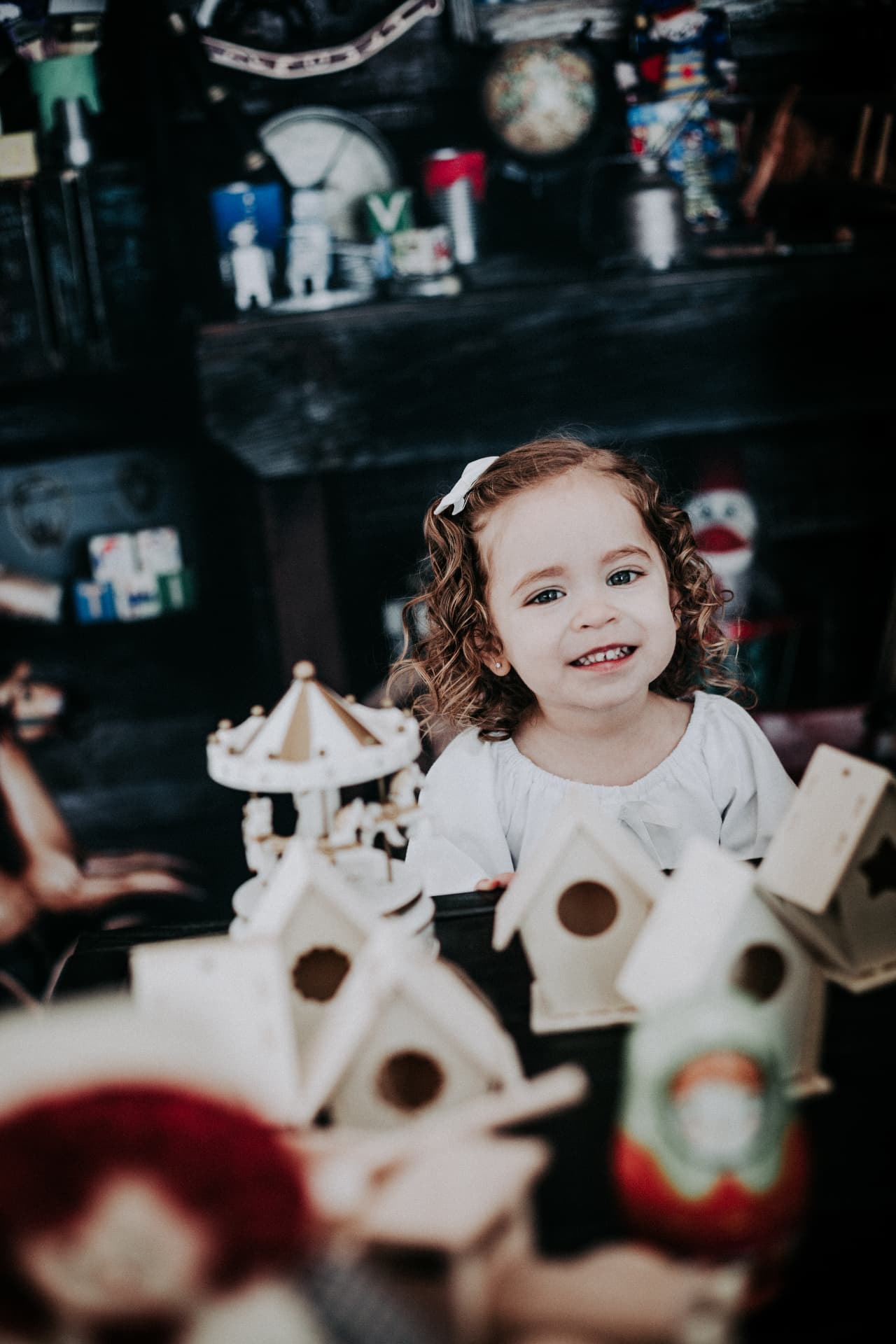 Curly-haired toddler smiling behind a row of hand-painted wooden birdhouses