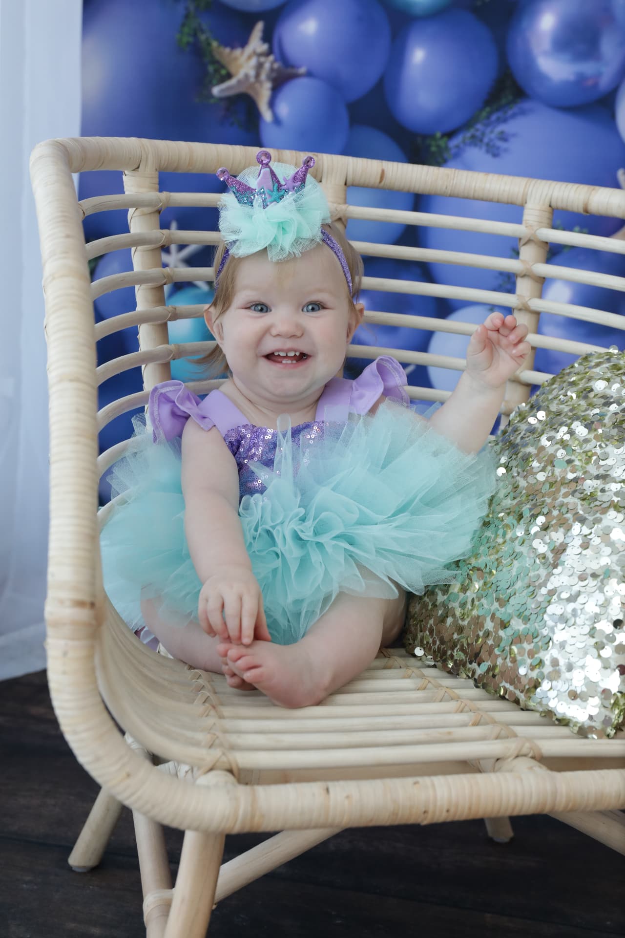 One-year-old in a mermaid tutu smiling in a rattan chair at her Smash & Splash session