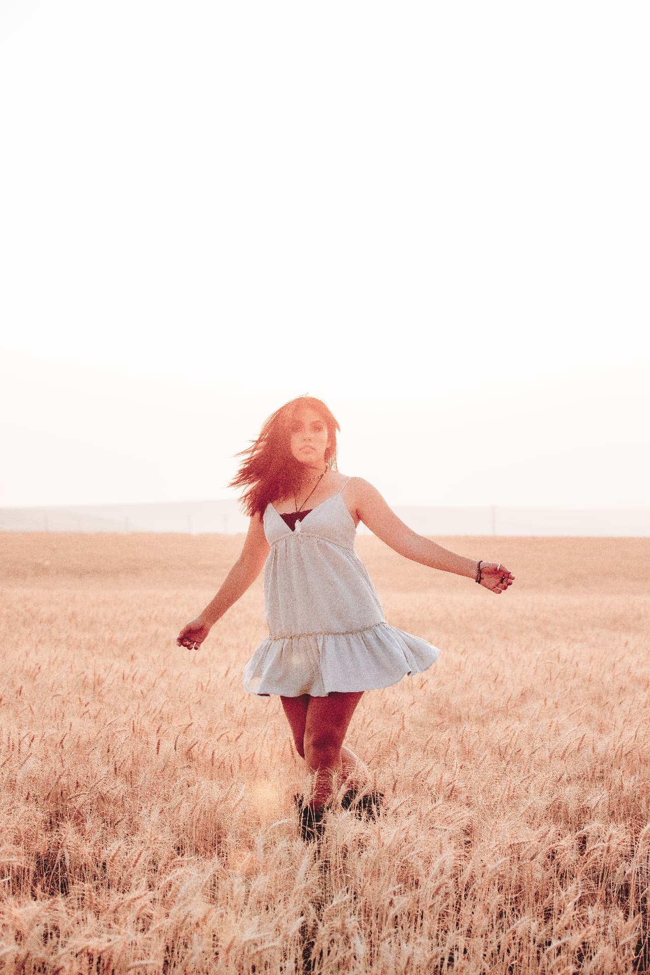 Senior twirling in a light dress in a wheat field at golden hour