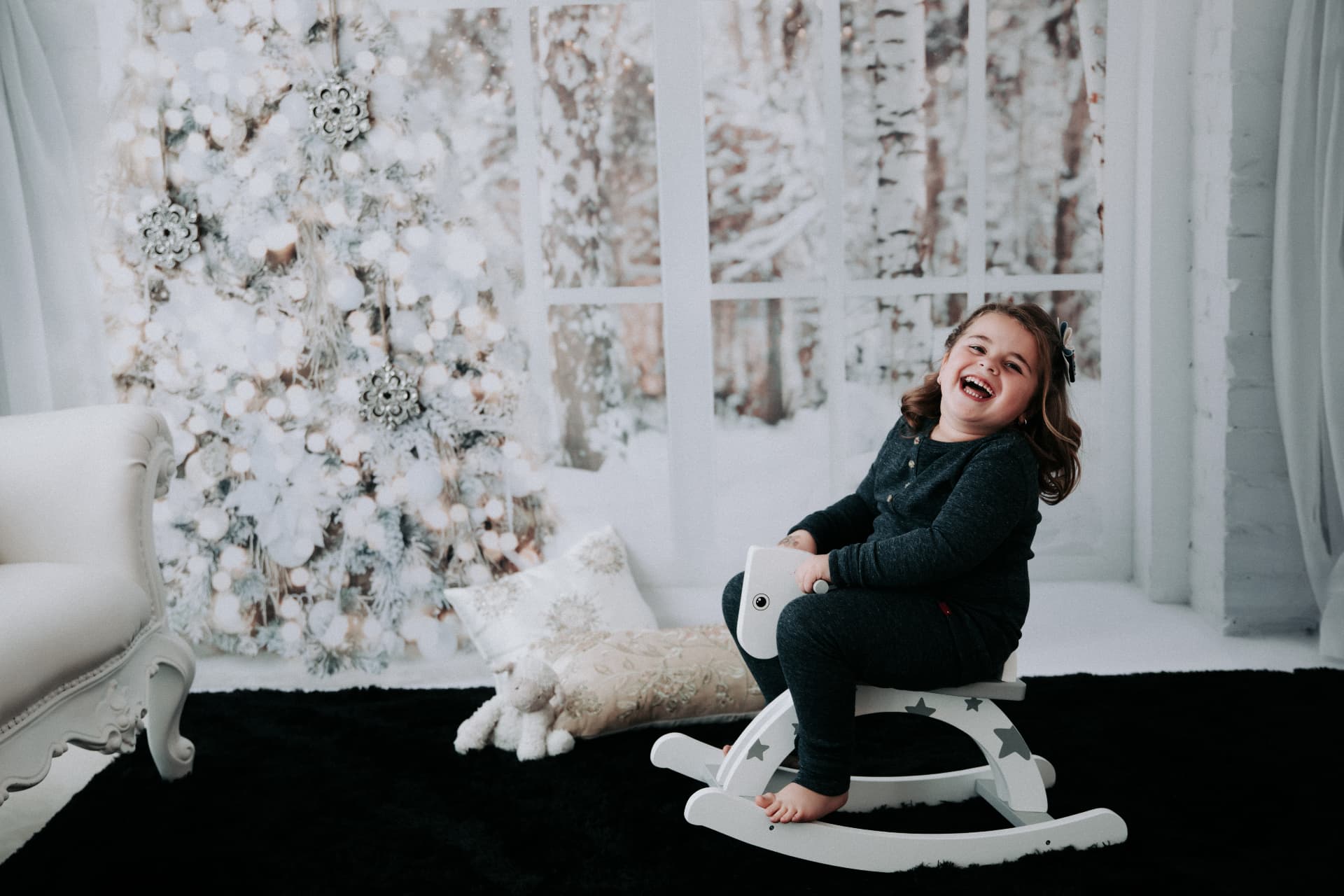 Child laughing on a white rocking horse in a snowy white Christmas set
