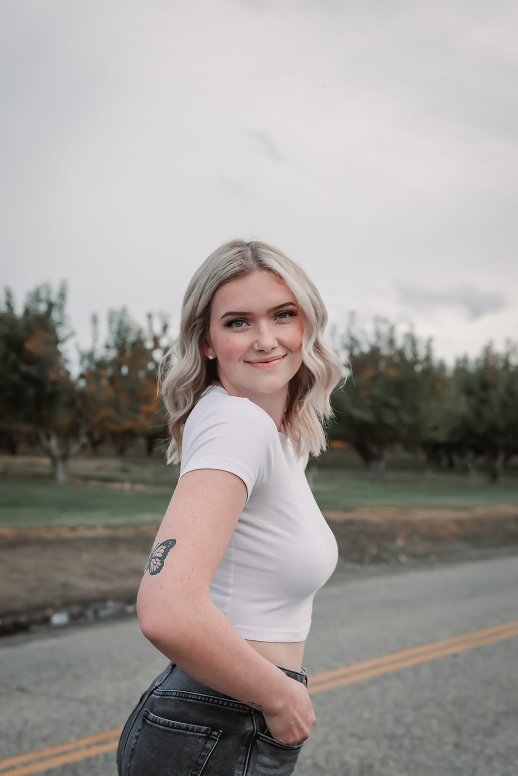 Senior in a white tee on a country road lined with orchard trees