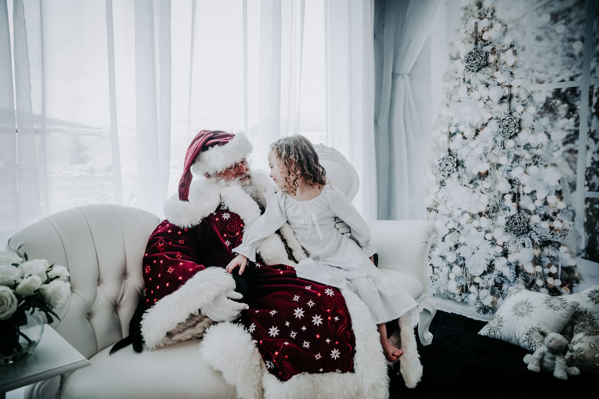 Santa and a little girl talking on a white sofa in the winter white set