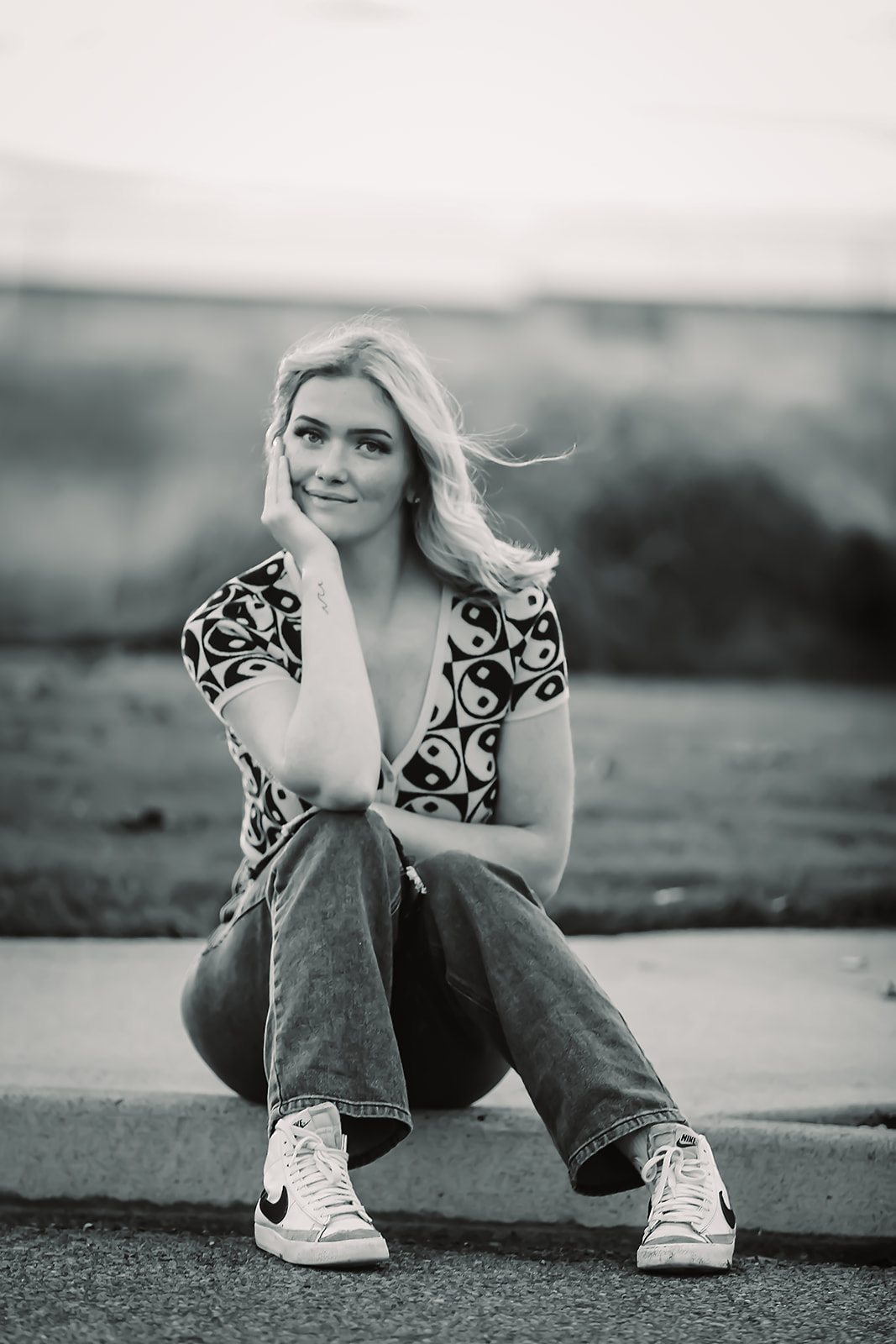 Black and white senior portrait seated on a curb in wide-leg jeans