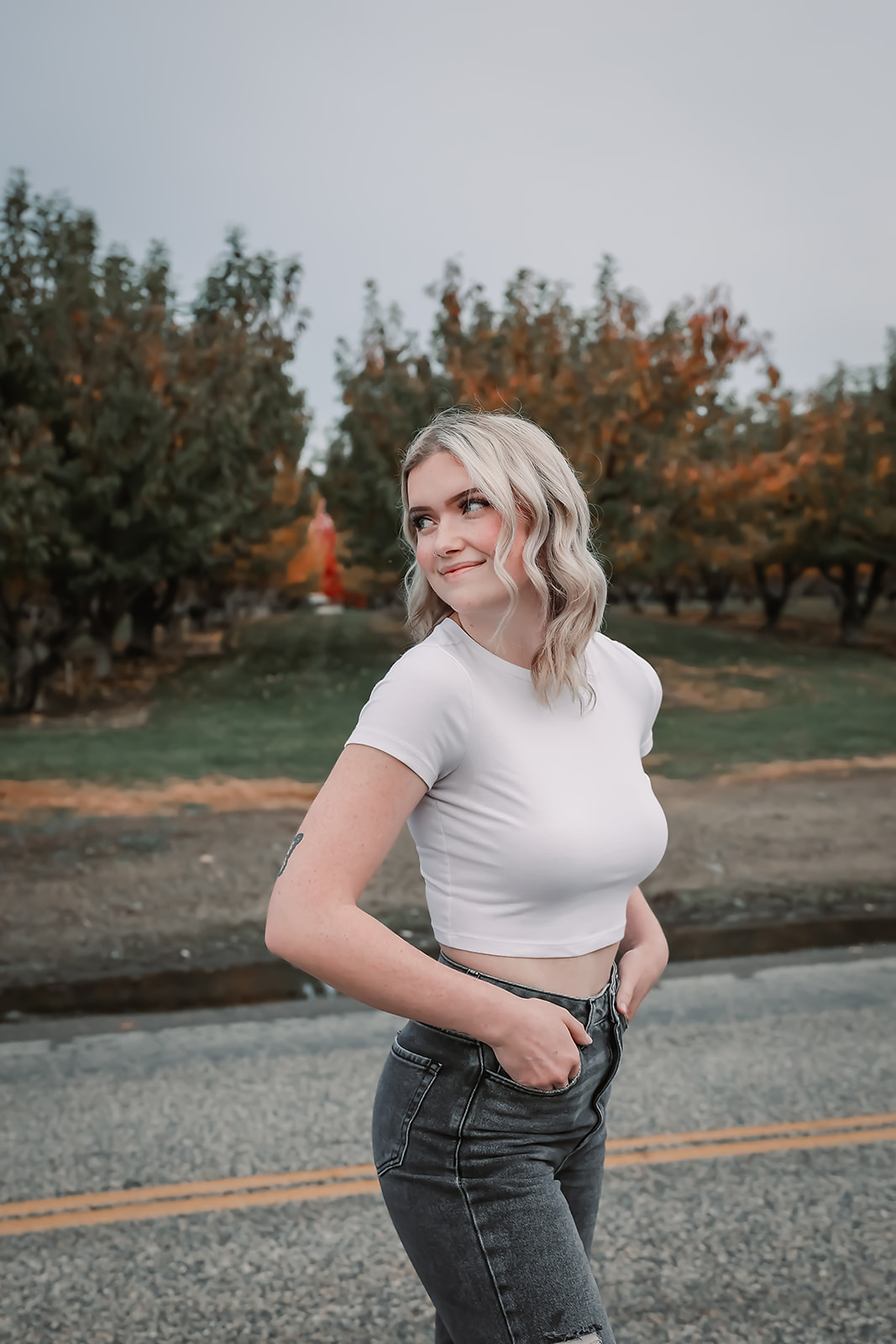 Senior laughing on an orchard road in a white tee and black denim