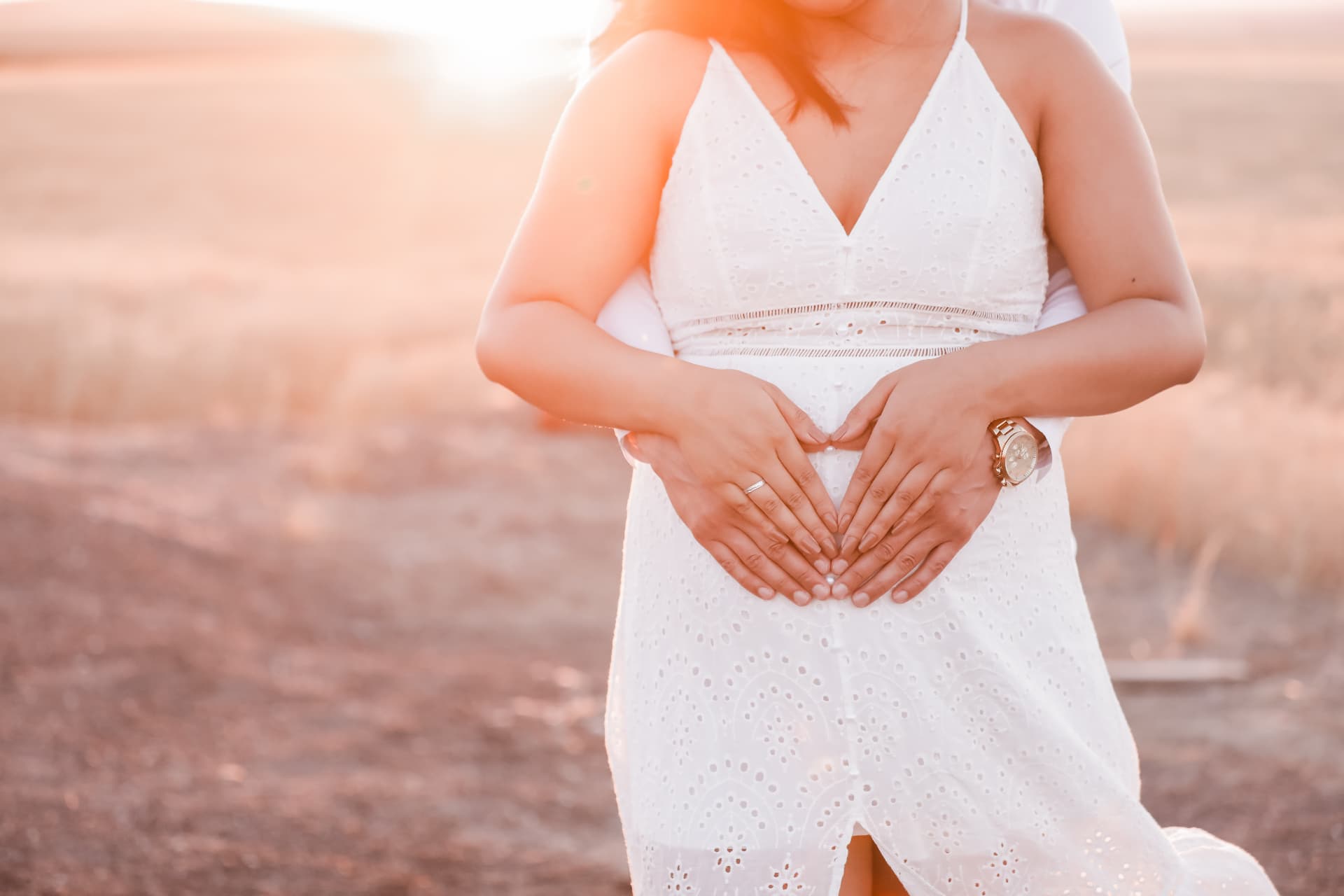 Hands forming a heart over the bump in golden sun flare