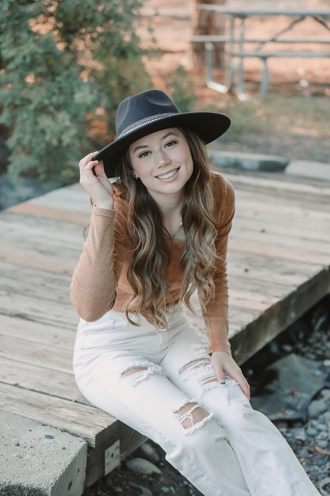 Senior tipping her black hat while seated on a wooden bridge