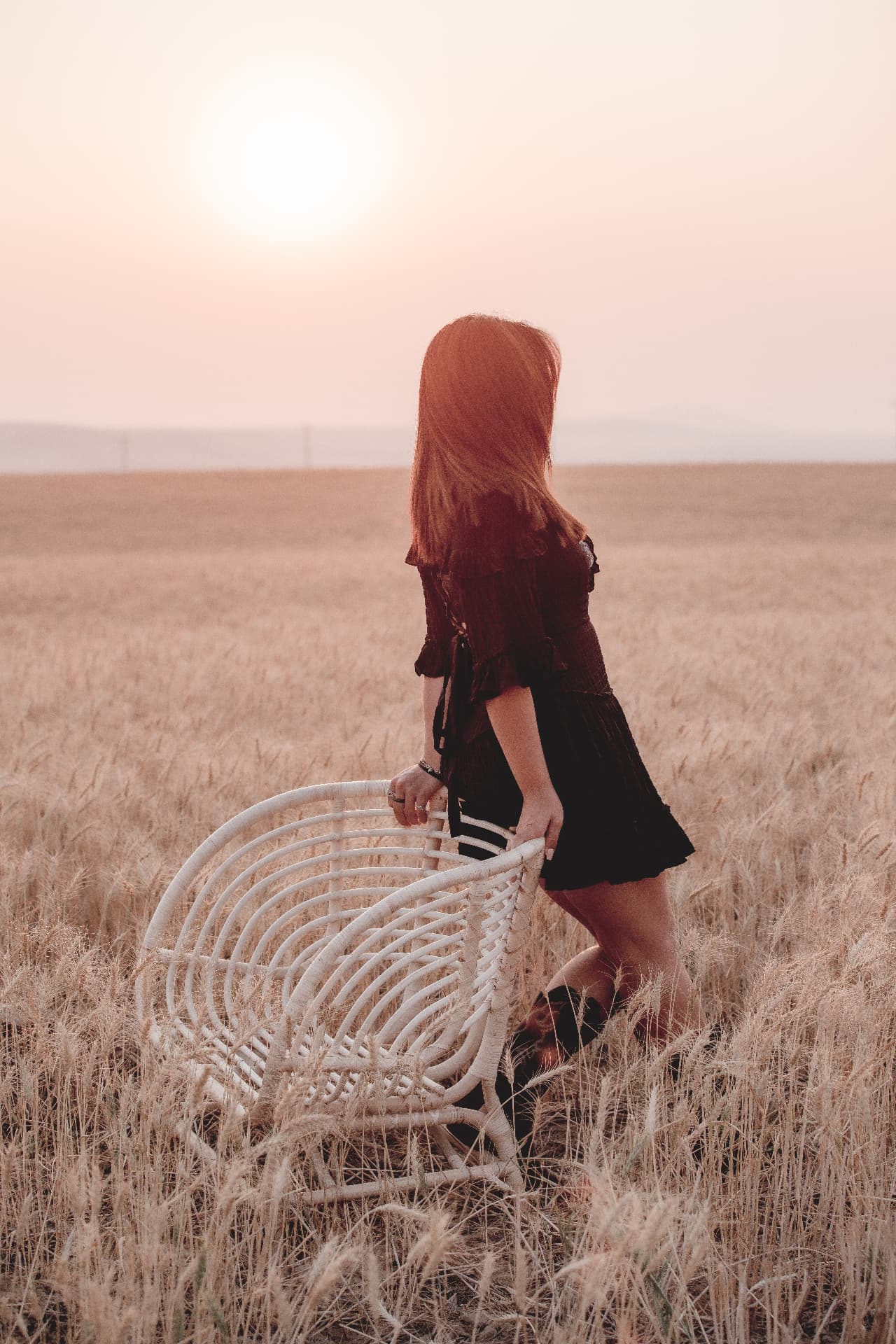 Senior in a black dress in a golden wheat field at sunset