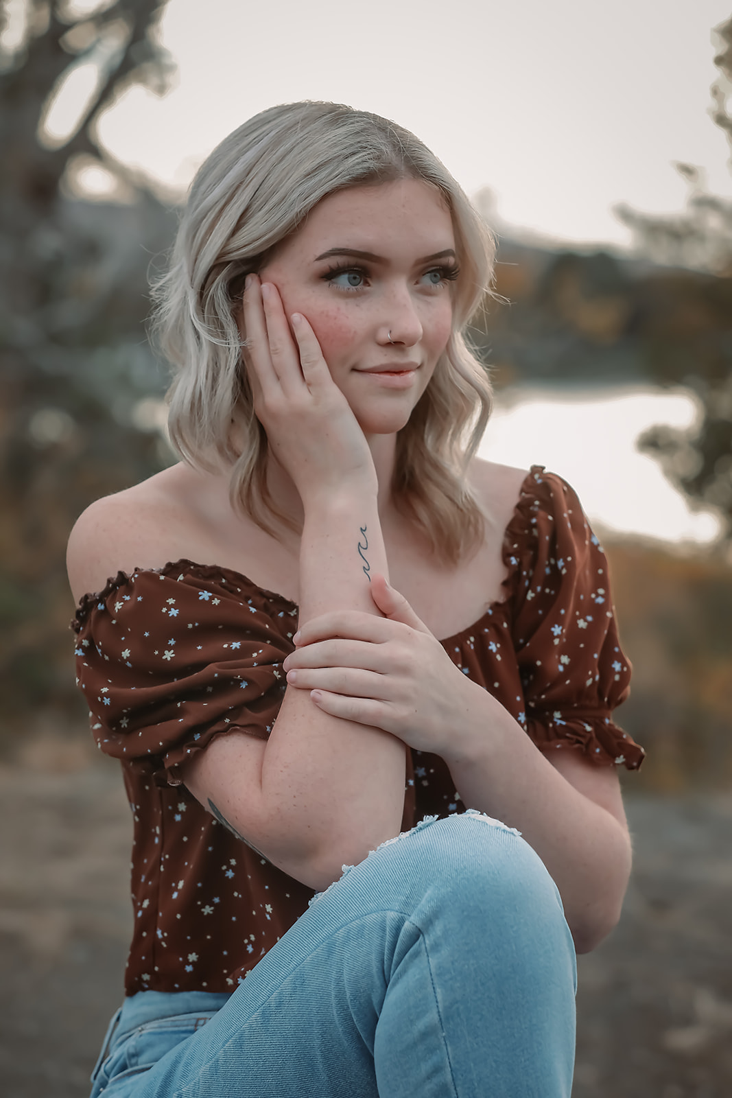 Senior in a floral off-shoulder top seated by the water at sunset