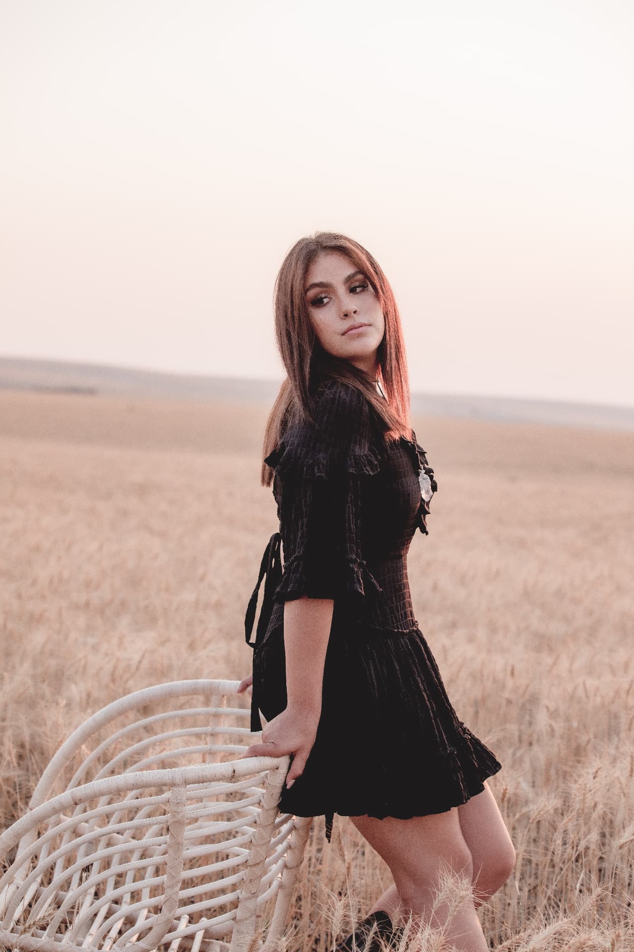 Senior leaning on a white rattan chair in a wheat field