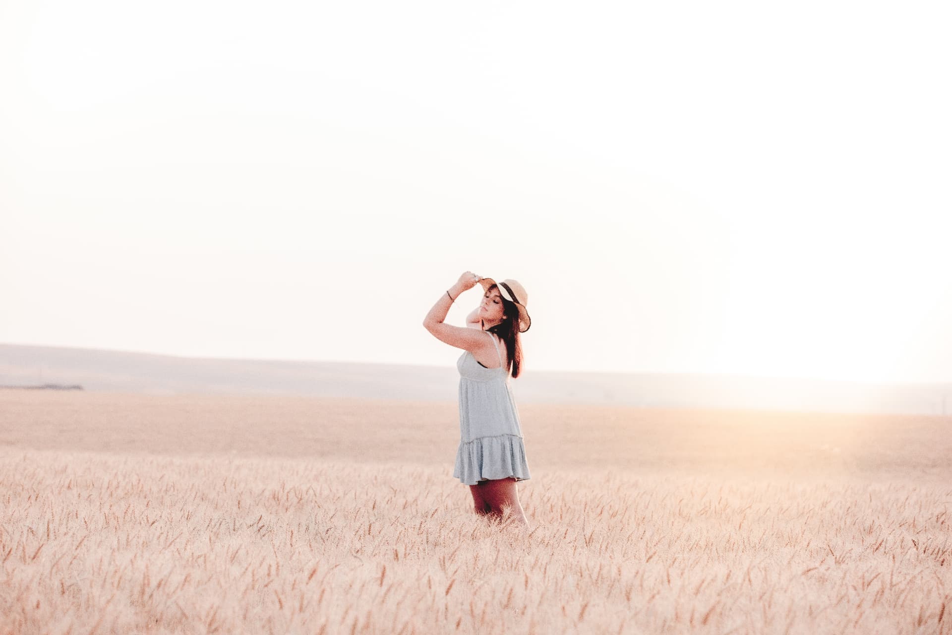 Senior in a straw hat standing in a sunlit wheat field