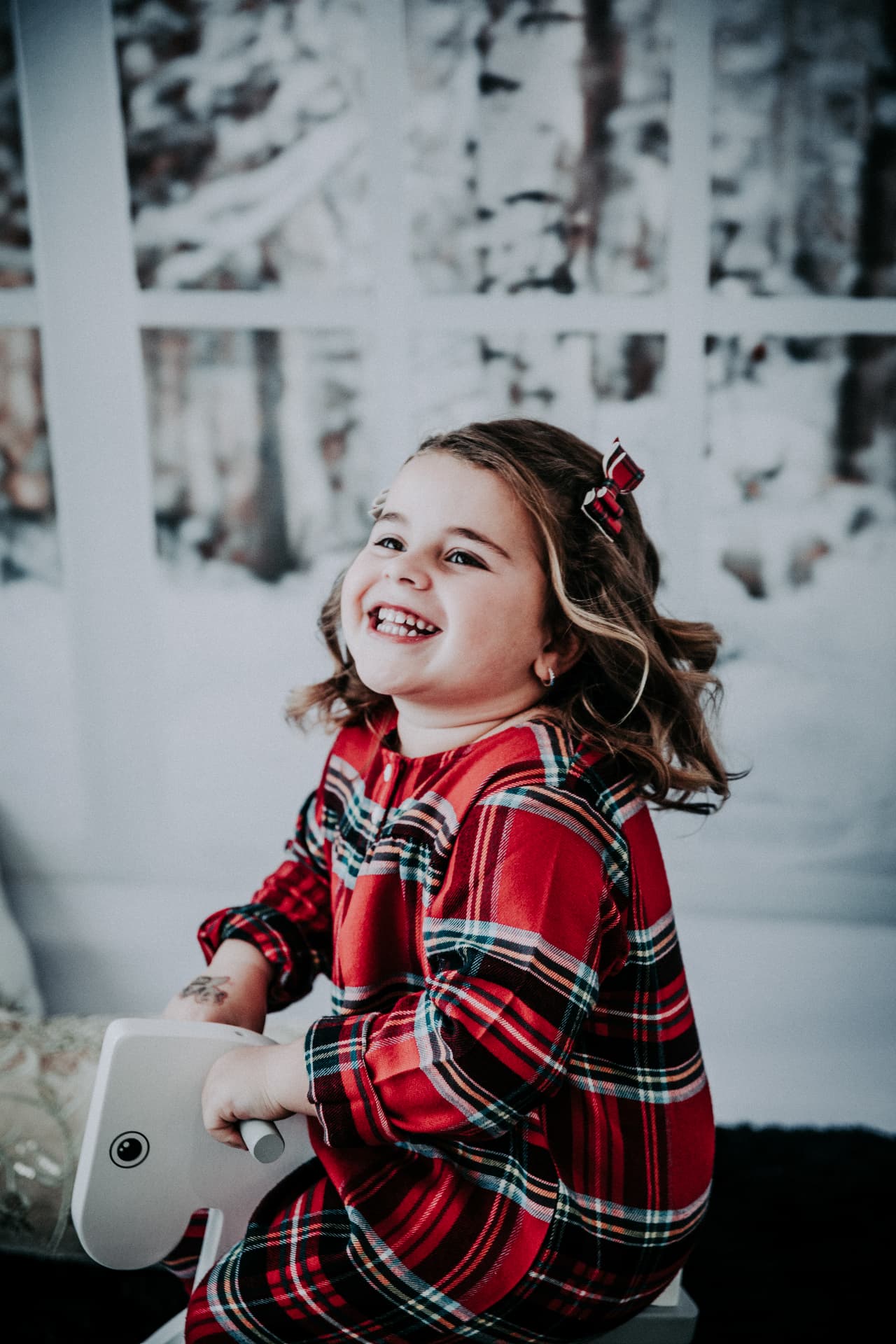 Little girl in red holiday plaid laughing on a white rocking horse
