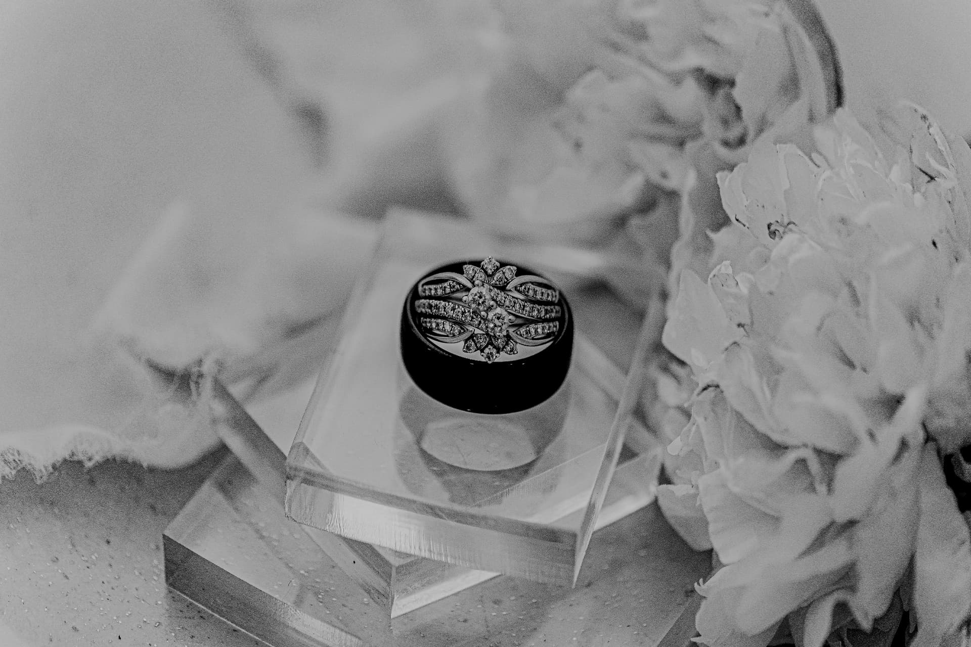 Black-and-white editorial close-up of a bride's diamond wedding ring set nestled among ivory peonies
