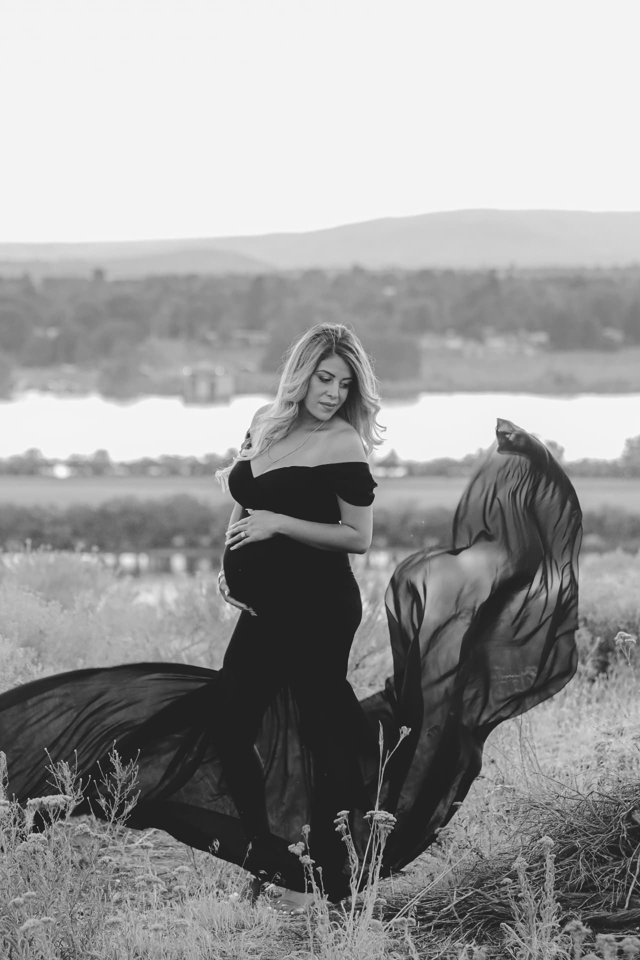 Black and white maternity portrait in a flowing gown by the river